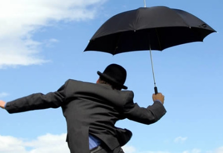 Man with umbrella, under sunny sky, jumping for joy.